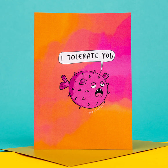 funny pink and orange A6 greeting card featuring a pink puffer fish illustration pulling a bored and fed up expression. The card has a pairing gold envelope. Designed by Katie Abey.
