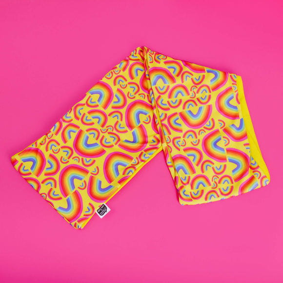 The Rainbow Jersey Circle Scarf on a bright pink background. The yellow scary has rainbow illustrations all over by Katie Abey 
