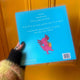 back of the book with a sky blue cover and white text blurb with illustration underneath of axolotl playing the saxophone. 