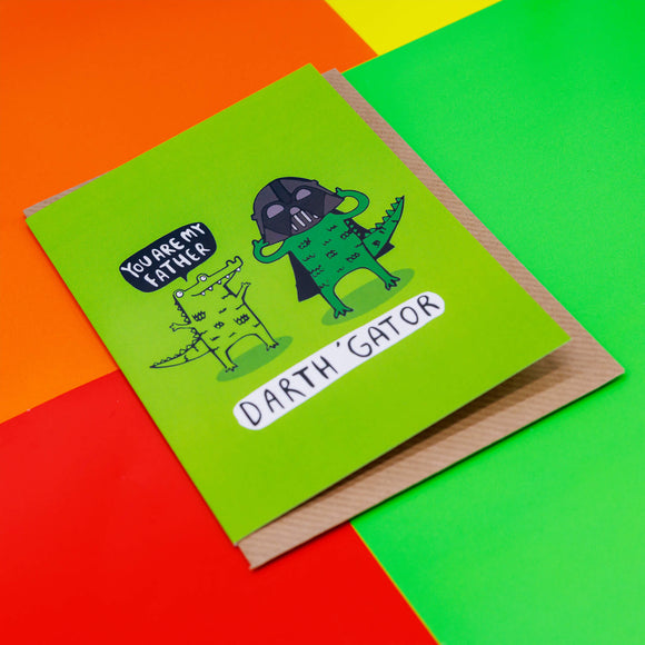 Darth Gator a6 greetings card designed and printed by Katie Abey in the UK. The card cover is neon green with two alligators, one is saying 'you are my father' and the other one is wearing a darth vador helmet and cape. The text underneath them reads 'darth 'gator'.