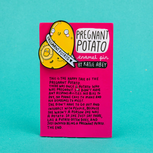 enamel pin badge shaped like a potato with a mini potato in its belly space and a banner around it that says pregnant potato. It is on a pink backing card telling the tale of the potato illustrated by Katie Abey