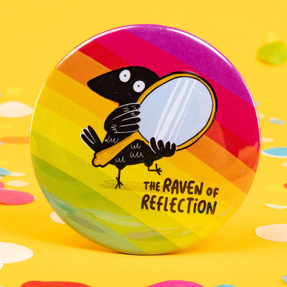a circular shaped rainbow coloured pocket mirror with the raven of reflection on the front illustrated by Katie Abey