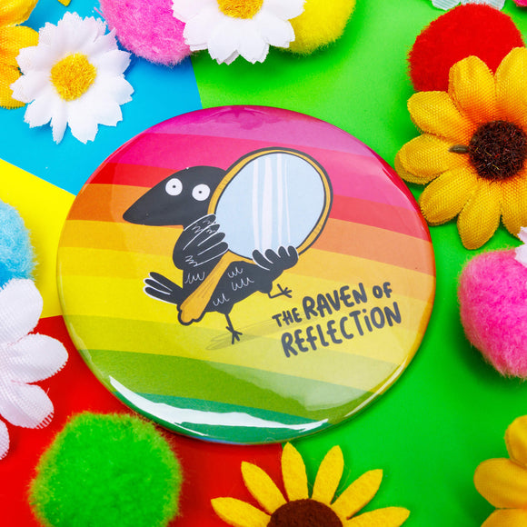 a circular shaped rainbow coloured pocket mirror with the raven of reflection on the front illustrated by Katie Abey