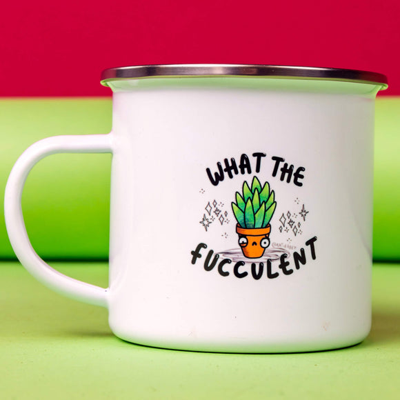What The Fucculent Enamel Mug sat in front of a lime green and red backdrop. The white mug with silver brim has an illustration of a green succulent in a pot with a twitch in it's eye and down turned mouth. Sparkles are drawn either side of the succulent. The text on the mug reads what the fucculent. Designed by Katie Abey in the UK.