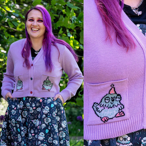Front and back views of the Rebel Romance x Katie Abey Pigeon Party Cardigan. This vegan friendly lilac cardigan features embroidered party pigeons on the front pockets, colourful buttons and a large pigeon holding a blue balloon knitted into the back. Styled with the matching Pigeon Party Flared Pinafore Dress for a fun alternative look.
