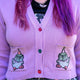 Close up of the Rebel Romance x Katie Abey Pigeon Party Cardigan in soft lilac knit. The cropped cardigan features colourful front buttons and embroidered party pigeons on both front pockets, making it the perfect cosy layering piece for quirky, colourful and alternative outfits.