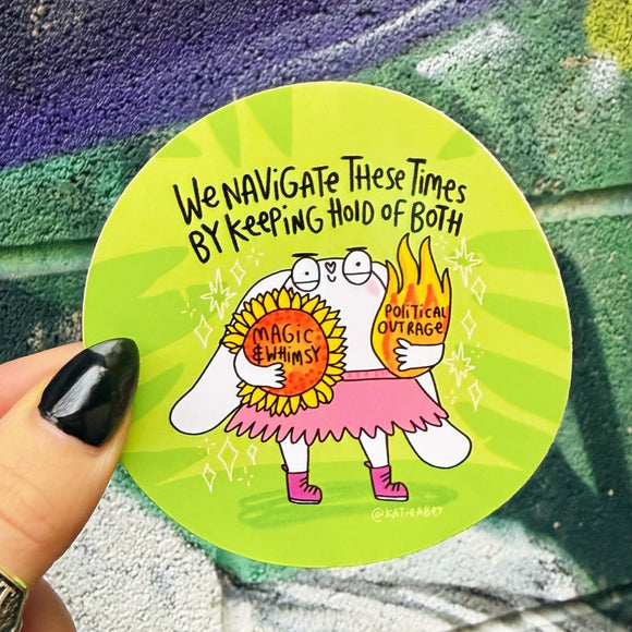 Bright green circular vinyl sticker illustrated by Katie Abey featuring a cute white character holding a sunflower labelled magic and whimsy and a flaming heart labelled political outrage. Handwritten text reads we navigate these times by keeping hold of both. Bold, playful illustration with sparkles, pink skirt and boots, celebrating balance, feelings and being unapologetically weird.