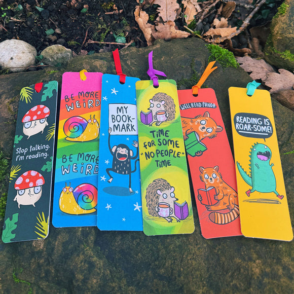 Collection of colourful Katie Abey illustrated bookmarks displayed outdoors on a stone wall. Time For Some No People Time hedgehog bookmark shown alongside other quirky animal and reading themed designs. Bright, bold colours with ribbon ties. Fun, weird and wonderful gift stationery for book lovers and introverts.
