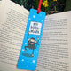 Blue “My Bookmark” Monkey Bookmark by Katie Abey placed inside an open book outdoors. The illustrated monkey holds a sign reading “My Book-mark” against a starry blue background with a red ribbon tie. Laser printed on sturdy card with a premium silk finish. A colourful, quirky bookmark from small UK illustrator Katie Abey, perfect for book lovers who like to be more weird.
