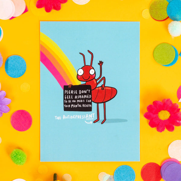 A6 postcard of a smiling ant waving on arm in the air holding a sign that says 'Please don't feel ashamed to be on meds for your mental health' under the sign it says 'The AntidressANT' it is drawn on a blue background with a rainbow. 