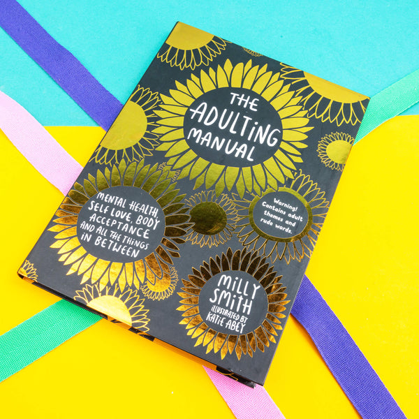 front cover of the Adulting Manual by Milly Smith illustrated by Katie Abey. It has lots of gold shiny flowers on a black background