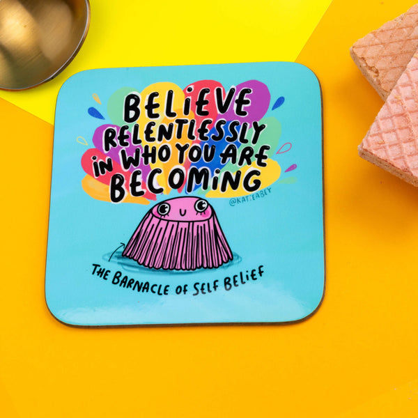 blue coaster with an illustration of a barnacle by Katie Abey with Believe relentlessly in who you are becoming written on the top and The Barnacle of self Belief written underneath.