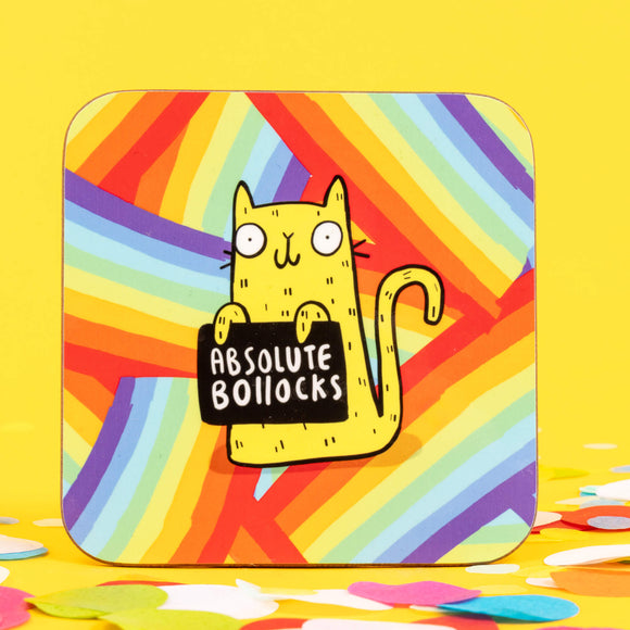 a coaster of a yellow cat on a rainbow striped background smiling holding a sign saying 'ABSOLUTE BOLLOCKS'