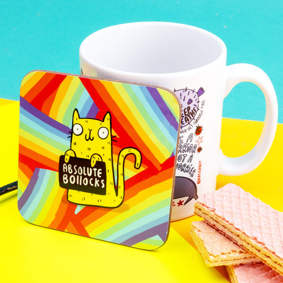 a coaster of a yellow cat on a rainbow striped background smiling holding a sign saying 'ABSOLUTE BOLLOCKS'