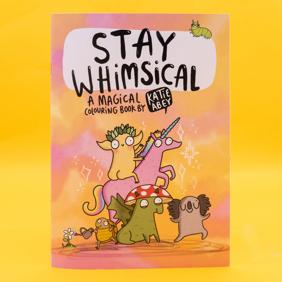 A5 colouring book cover titled “Stay Whimsical – A Magical Colouring Book by Katie Abey.” Features quirky illustrated characters: a leafy creature riding a pink unicorn, a mushroom-hatted dragon, a koala, and a bug watering flowers, all on a dreamy pastel background. A fun and magical book encouraging joy and weirdness.