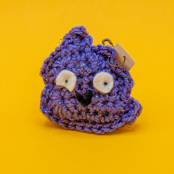 Front view of the Galactic Poo Crochet Pal by Katie Abey, a handmade purple crochet plush character with felt eyes and sparkly yarn. This small novelty crochet toy is vegan friendly and stuffed to keep its shape. A fun quirky gift inspired by Katie Abey’s galactic poo illustration and crafted with Forest Folk Crochet.