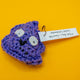 Handmade crochet Galactic Poo character plush by Katie Abey, featuring large felt eyes and a cheeky smile. Made with purple sparkly vegan yarn and lightly stuffed to hold its shape. A small novelty crochet toy created in collaboration with Forest Folk Crochet, perfect as a quirky gift for lovers of weird and whimsical art.