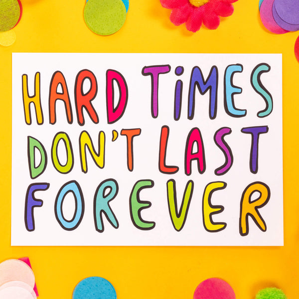 A postcard with rainbow letters in capitals saying hard times don't last forever it is white and on a yellow background with confetti, daisies and pom poms.