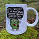 White ceramic affirmation mug sitting on mossy ground with a soft outdoor background. The mug features a cute green illustrated character and bold hand lettered text saying “No offence, but you are more loved than you can ever comprehend”. Ethically produced and designed in the UK by Katie Abey.