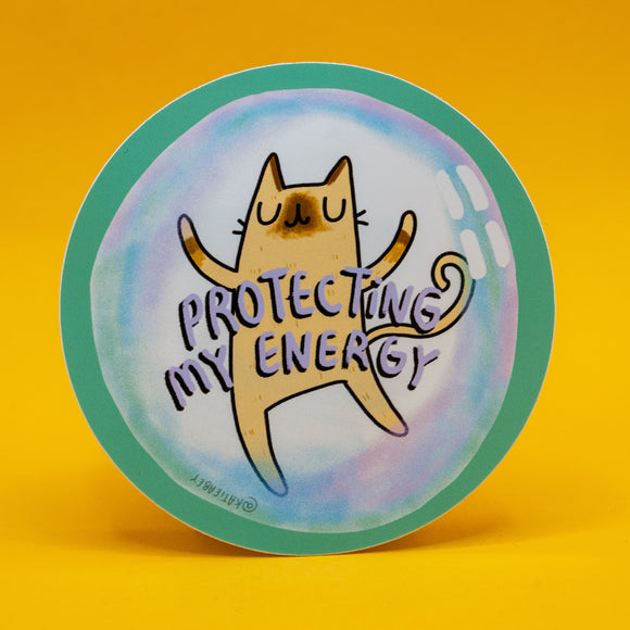 Round vinyl sticker featuring a cute illustrated cat with closed eyes inside a pastel protective bubble, with the words “Protecting My Energy” in bold purple lettering. Designed by UK illustrator Katie Abey, this quirky 8cm waterproof vinyl sticker encourages self care, boundaries and embracing your weirdness. Ideal for laptops, water bottles, journals and planners.
