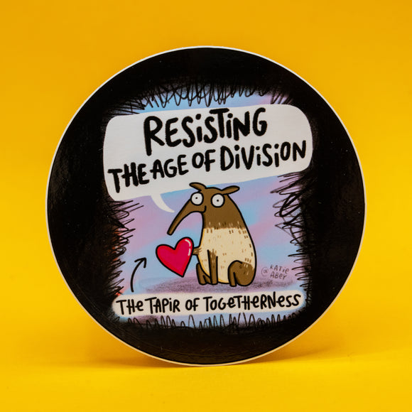 The Tapir Of Togetherness vinyl sticker by Katie Abey featuring a cute illustrated tapir holding a red heart with the words “Resisting the Age of Division”. Round sticker with black border and pastel background. Approx 8cm waterproof vinyl sticker, wipes clean, perfect for laptops, notebooks and water bottles. Quirky gift from UK illustrator encouraging you to be more weird.