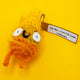 Spark Of Hope Crochet Pal handmade soft toy by Katie Abey and Forest Folk Crochet, a small fluffy orange and yellow crochet character with big googly eyes and tiny legs, inspired by the “Keeping My Tiny Spark Burning” illustration. Vegan friendly yarn plush mascot photographed on a bright yellow background, quirky alternative gift for fans of cute weird art and handmade crochet creatures.
