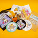 Contents of the Box of Brilliance by Katie Abey of January's theme, Protect Your Energy, three postcards with katie abey artwork, a flame artwork coaster, a crochet flame, protect my energy spell bottle, relaxing and magical bath salts and three stickers. 