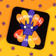 Katie Abey coaster with a quirky purple bat illustration and fun text saying 'Everyone Sucks Apart From You' in white. The background shows colourful orange and purple petal shapes. Purple spider confetti is sprinkled on the vibrant orange surface. Katie Abey encourages embracing your weirdness with lighthearted, fun designs.