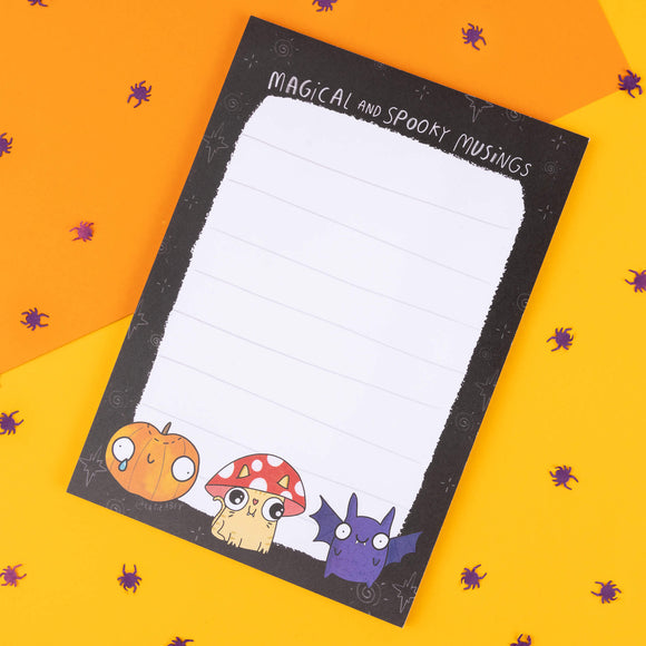 A colourful Katie Abey notepad with 'Magical and Spooky Musings' text at the top. Illustrated with a pumpkin, mushroom, and bat character at the bottom, surrounded by a black border with magical accents. Ideal for creative writing, journaling, or adding some weird to your desk.