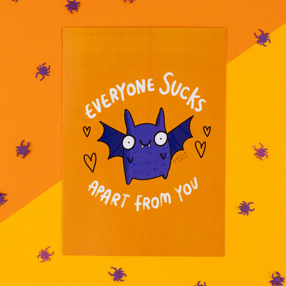 A quirky, vibrant Halloween-themed postcard by Katie Abey, featuring a cute purple bat with wings spread wide and a goofy expression. The text "Everyone Sucks Apart From You" is displayed in bold white letters around the bat. The background is bright orange, with scattered purple spider confetti for a playful spooky effect. Perfect for gifting to someone special who loves fun, weird illustrations and a bit of dark humour.