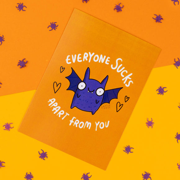 Katie Abey’s Halloween-inspired postcard, featuring an adorable purple bat with wide, happy eyes and outstretched wings. The text "Everyone Sucks Apart From You" wraps around the bat in bold white letters. The postcard sits on a bright orange background scattered with purple spider confetti, adding to the quirky, spooky vibe. Ideal for gifting to someone who enjoys fun, offbeat humour and the weirdness of Katie Abey’s artwork.