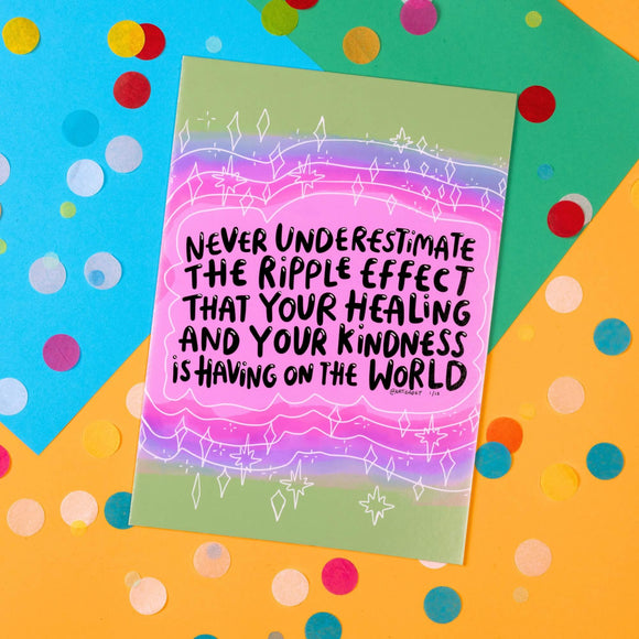 The Never Underestimate Yourself Art Print on a blue, green and yellow card background with rainbow circle confetti. The art print has a pink, purple and green gradient with white sparkles and lines surrounding black text reading 'never underestimate the ripple effect that your healing and your kindness is having on the word'. Under this quote is katie abey's signature with 1/15.