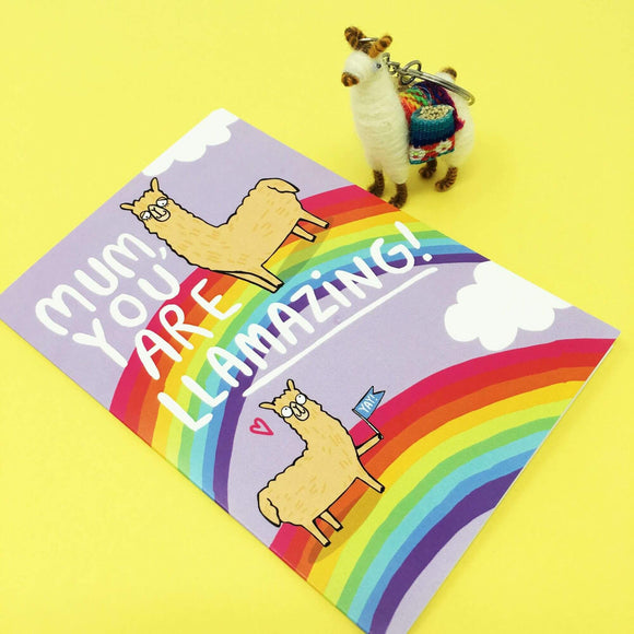 A6 Greetings Post Card Mothers Day that reads 'Mum, you are Llamazing!' with illustrated Llama's on rainbows and clouds on yellow background with a cute llama keyring sat next to it. Designed by Katie Abey in the UK