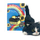 The Poobrain Cat Enamel Pin on its blue card backing with rainbows and sunflowers sat next to a toy cat. The enamel pin is of an open yellow box with a black cat inside with a silly expression. There is black text on the box that reads POOBRAIN. Designed by Katie Abey in the UK