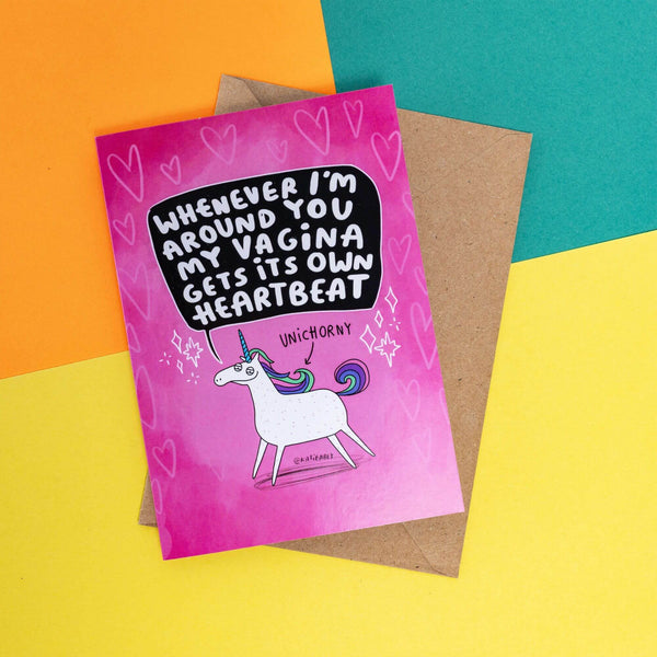  A sleazy looking white unicorn on a pink card with an arrow pointing to it saying 'UNIHORNY' Above that in a black speech bubble it says, 'Whenever I'm around you my vagina gets its own heartbeat.' It is on a pink card with hears and sparkles.
