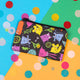 The Small Pets Coin Purse on yellow, blue and green card with rainbow circle confetti. The small black base coin purse has various colourful small pets such as chinchillas and rabbits with leaves and fruit all over and it has a black zip.