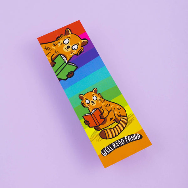Well read panda bookmark laying face up on a pastel purple background. The bookmark is laser printed card with a rainbow stripe background with two red pandas holding and reading books with bottom text reading 'Well Read Panda'. Designed by Katie Abey in the UK and printed with a silk finish so they are wipe clean.