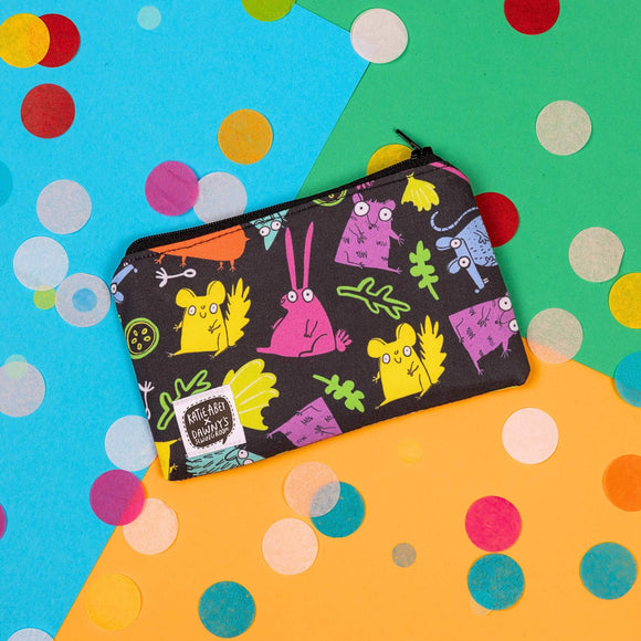 The Small Pets Coin Purse on yellow, blue and green card with rainbow circle confetti. The small black base coin purse has various colourful small pets such as chinchillas and rabbits with leaves and fruit all over, it has a black zip and a katie abey x dawny's sewing room tag in the bottom left corner.