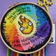 Finished cross stitch featuring a rainbow flame design, shown in an embroidery hoop with yellow scissors and thread tails underneath. Text reads “Tend to your spark.”
