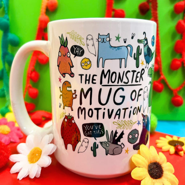  A colourful white mug from Katie Abey featuring a vibrant design of quirky, illustrated monsters and motivational quotes like "YAY!" and "You've got this!" against a bright green background with red and pink pom-pom decorations.