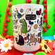 Katie Abey's fun and colourful mug adorned with whimsical monsters and motivational phrases like "Keep doing the thing!" and "YAY!" against a bright green background with cheerful floral decorations.