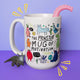 Katie Abey's white mug showcasing a lively collection of cute, illustrated monsters with positive messages like "The Monster Mug of Motivation" and "You've got this!" set against a purple background, with a dinosaur toy and pink tentacle adding extra charm.