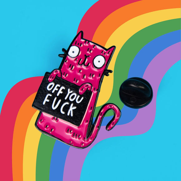 Close-up view of the Katie Abey soft enamel pin showing a pink cat holding a black sign with the phrase 'Off You Fuck'. The pin is set against a blue background with a rainbow arch, highlighting the playful and humorous design.