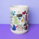 A white mug designed by Katie Abey featuring a delightful mix of quirky monsters and uplifting quotes, such as "Keep doing the thing!" and "Keep your chin up," with a lavender background highlighting the playful design.