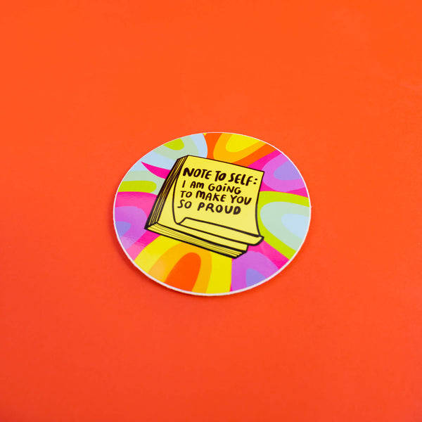 Circular sticker with rainbow pattern and featuring a yellow pile of post it notes which read 'Note to self: I am going to make you so proud' in black writing. Designed in the UK by Katie Abey