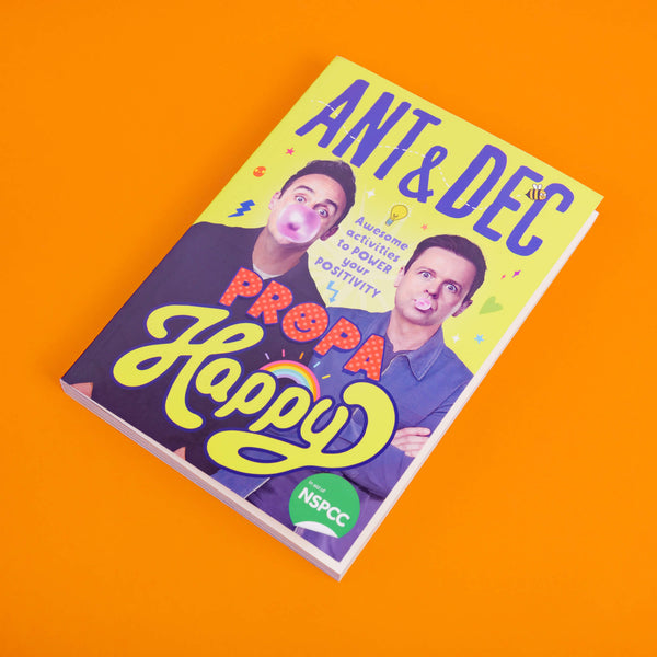 Propa Happy by Ant & Dec Illustrated by Katie Abey. The yellow book has a photo of Ant and Dec on the front cover blowing bubbles with pink bubblegum. The text reads Ant & Dec Propa Happy - awesome activities to power your positivity. There are little Katie Abey draws dotted around the cover such as stars, hearts and lightening bolts