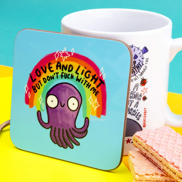 Love and Light but don't fuck with me circular pale blue square coffee tea coaster, featuring purple smiley octopus with rainbow and stars, and black writing. Designed by Katie Abey in the UK