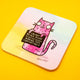 Angled product photo of the Katie Abey “I’m Not Being Rude” coaster featuring a pink illustrated cat holding a cheeky sign. The 9cm square coaster has rounded edges, a pastel background, and sits on a vibrant yellow surface. A fun and durable British-made coaster perfect for adding personality to your home or office.