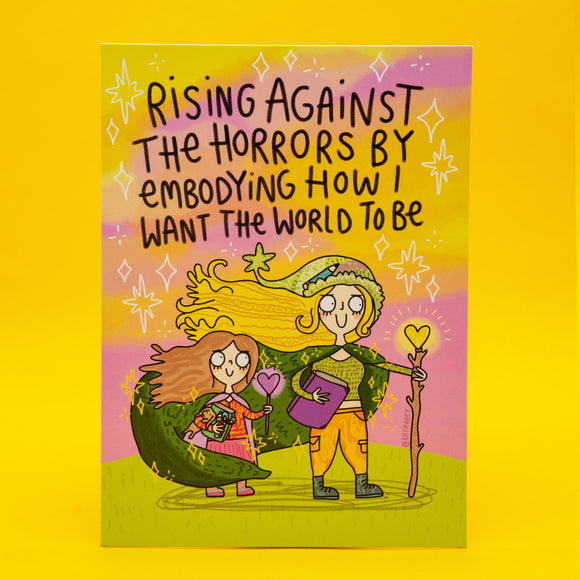 A6 size illustrated postcard by Katie Abey featuring two whimsical characters of a mum and daughter standing together under a pink and yellow sky with sparkles. One holds a glowing heart wand and book, the other clutches a small object, both wearing green cloaks. Handwritten style black text reads “Rising against the horrors by embodying how I want the world to be”. Bright, magical and empowering artwork printed on silk card.