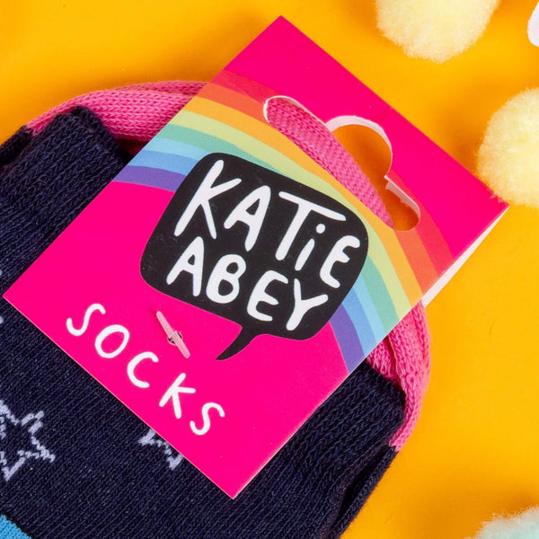 socks by Katie Abey with Axolotls in trans pride colours and stars with text saying don't tell me who I am on the front. The socks have pink toes and blue heels